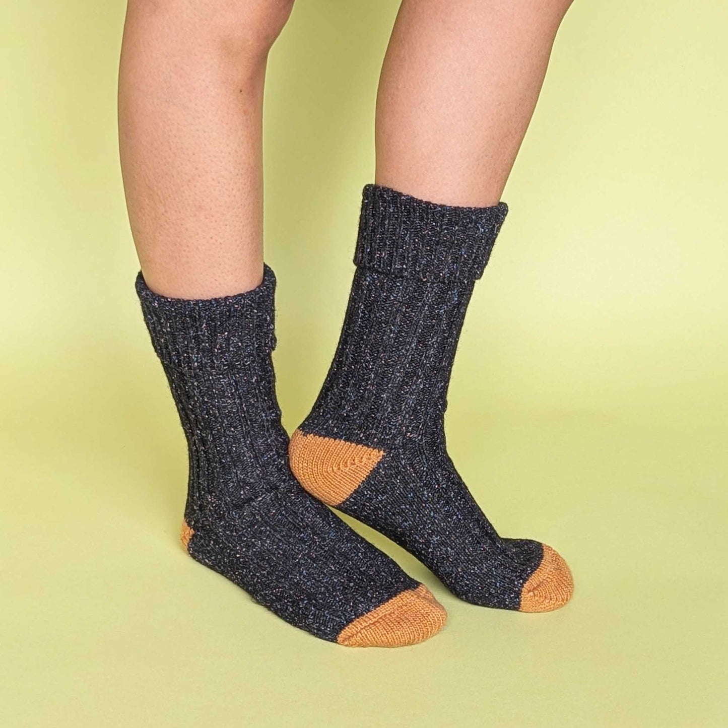 Dark gray socks with orange toes and cuffs worn by a person on a light green background