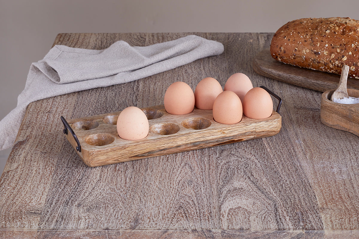 Eggs on a wooden tray with bread and a towel on a rustic wooden table