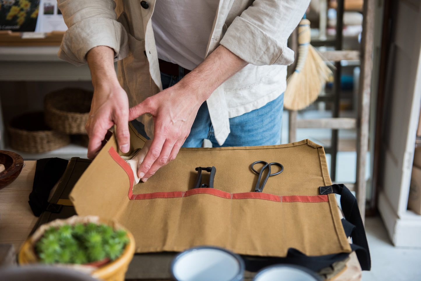 Person opening a mustard canvas garden tool roll with a beech stripe on a wooden table.