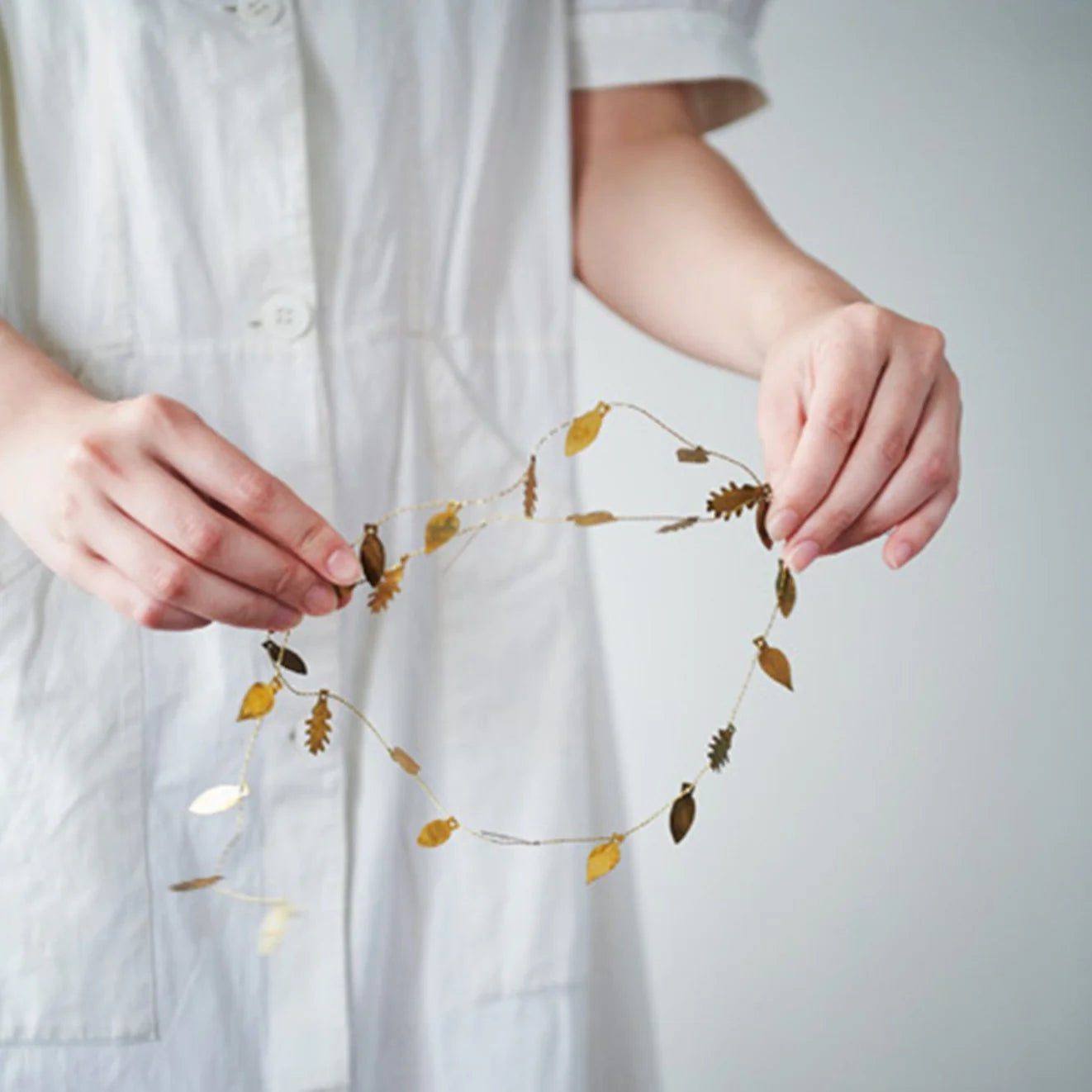 Person holding a Fog Linen Work leaf-shaped brass garland light against a white background