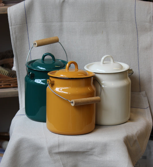 Three Ukrainian made enamel jars in teal, yellow, and white on a textured surface.