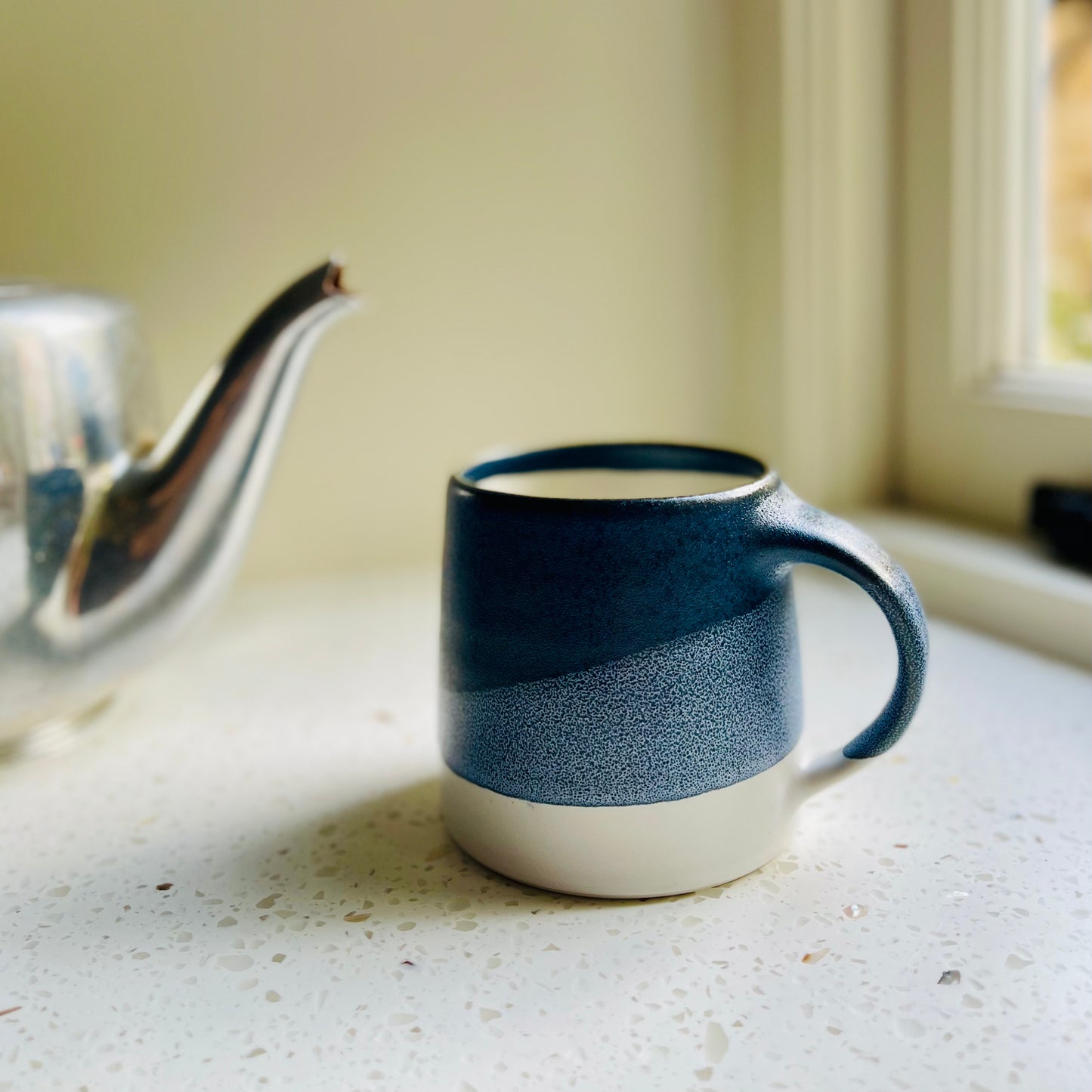 Blue and white ceramic KINTO mug on a windowsill with a teapot in the background