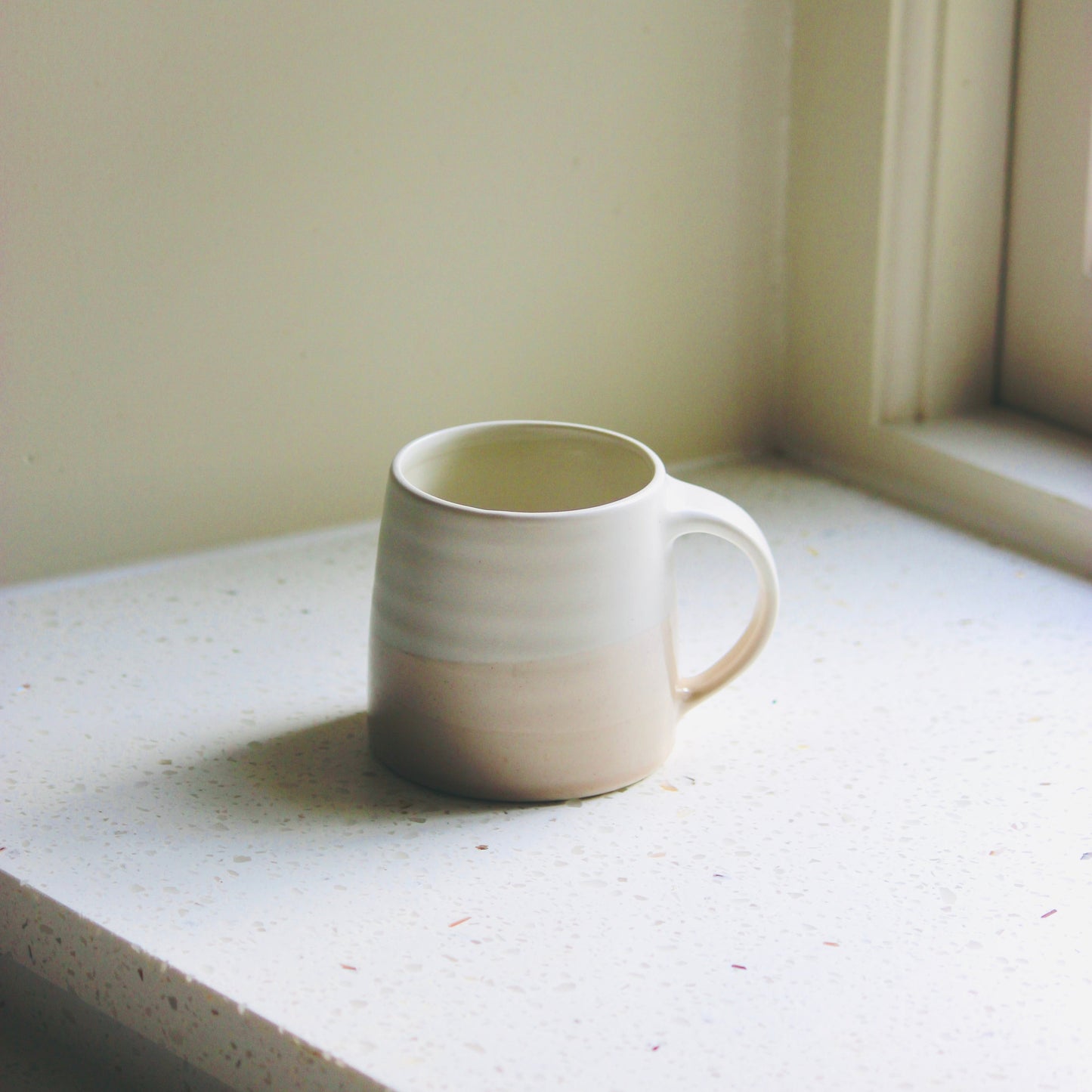 White ceramic KINTO mug on a windowsill with soft lighting
