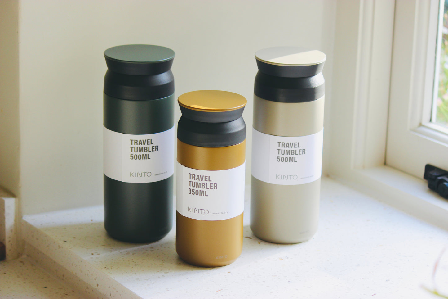 Three KINTO travel tumblers of different colours on a windowsill.