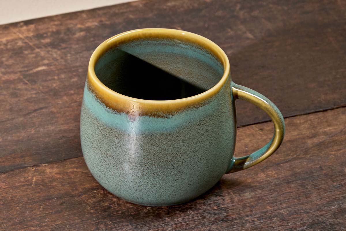 Teal blue Kalini mug from Nkuku with gold rim on a wooden surface