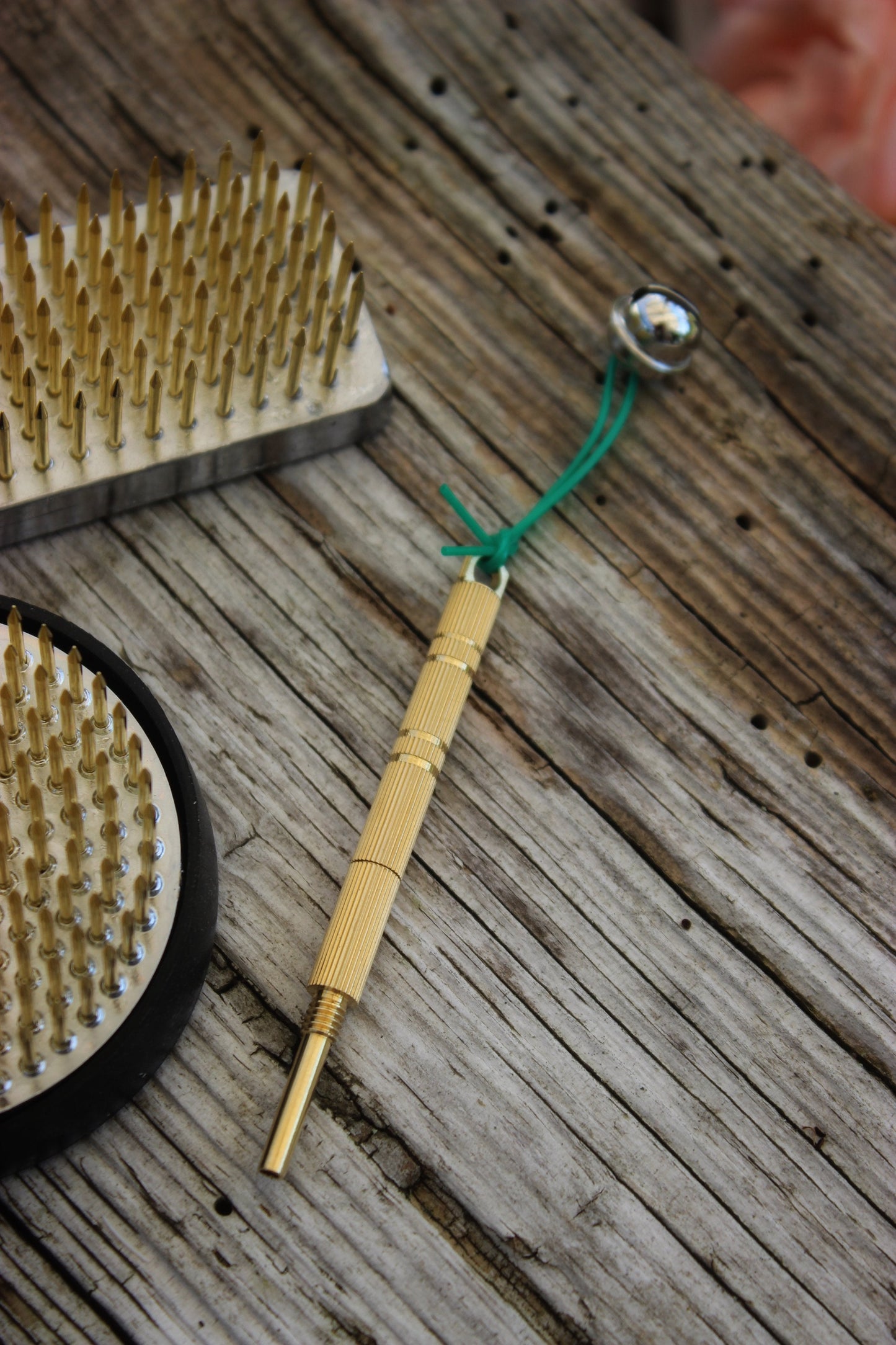 A brass Niwaki Kenzan straightener with a Japanese bell on a wooden surface.