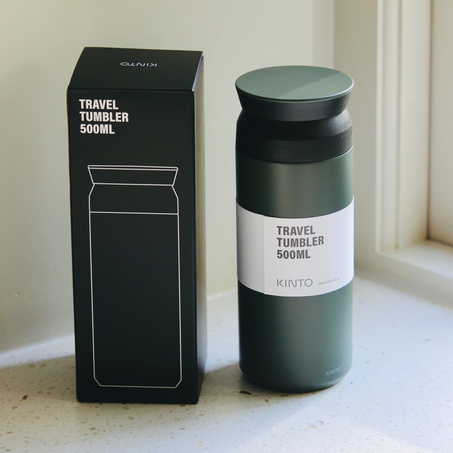 Ash Green Kinto travel tumbler with black lid and packaging on a light surface.