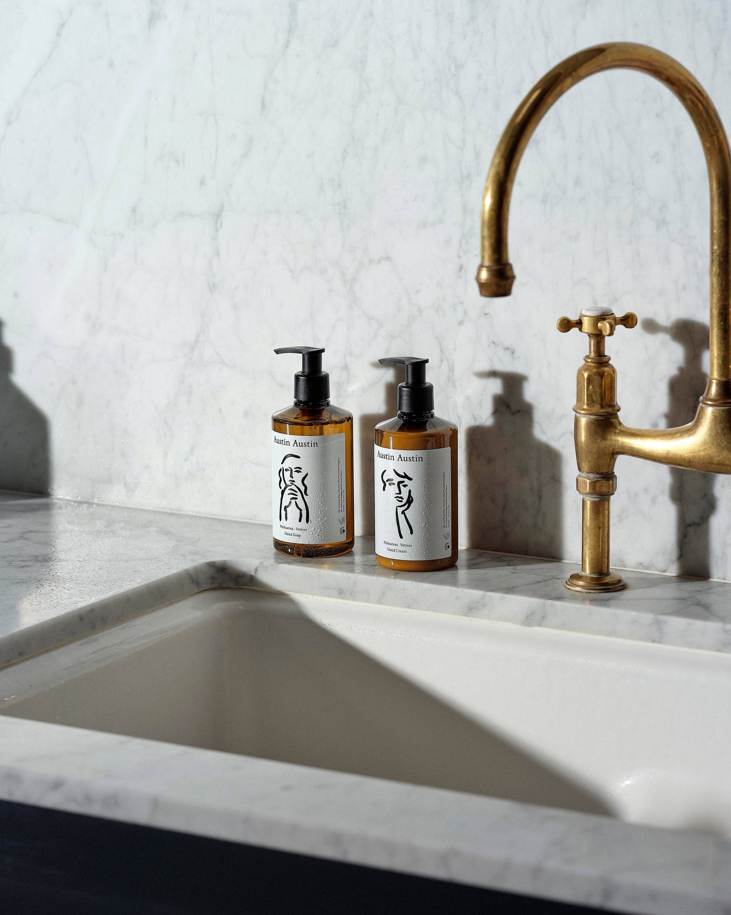 Two bottles of Austin Austin soap on a marble countertop with a gold faucet.