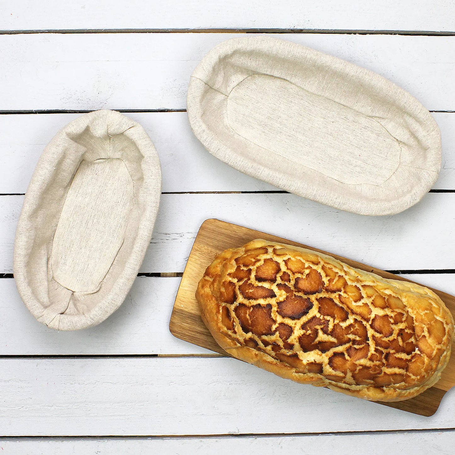 Two bread proofing baskets on a wooden surface with a loaf of bread on a cutting board.
