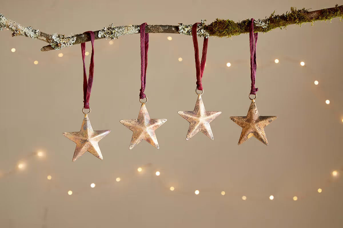 nkuku Rohani Star Baubles Set of Four Star-shaped ornaments hanging from a branch with a warm glow in the background