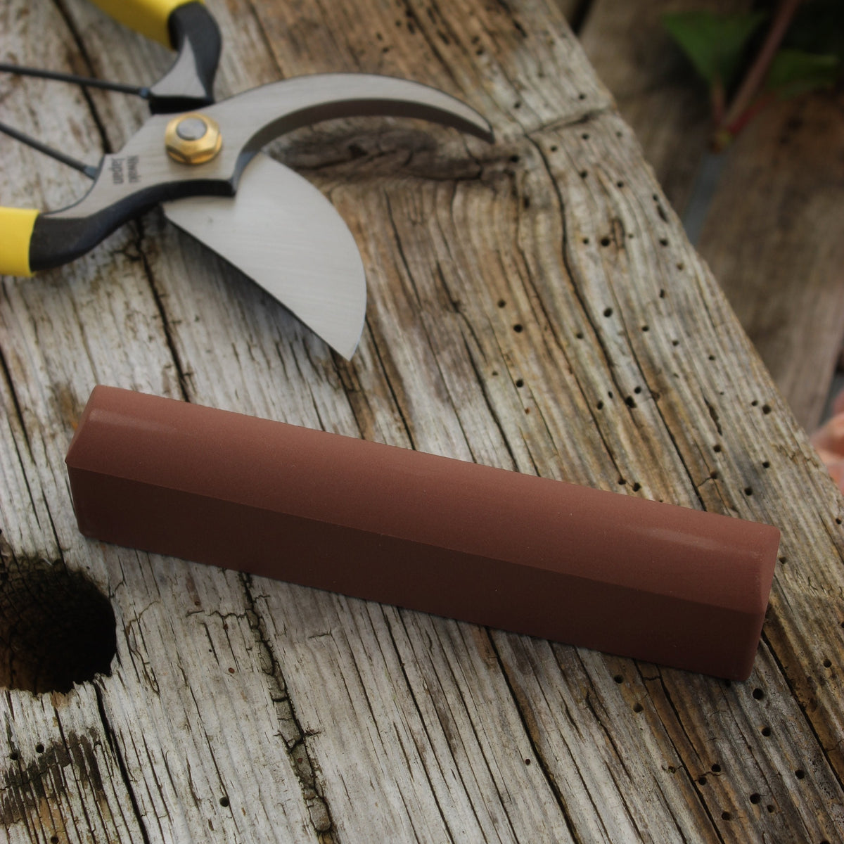 A brown sharpening stone placed on a wooden surface next to a pair of secateurs.