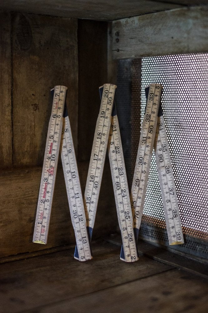 A traditional wooden folding ruler with imperial and metric measurements displayed, leaning against a wooden surface.