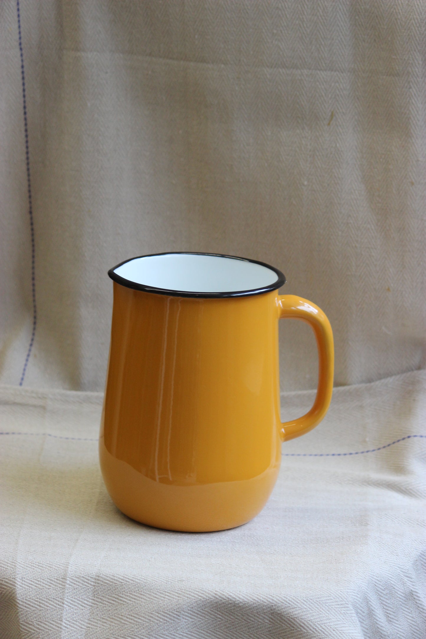 Yellow jug with a white interior on a beige fabric background