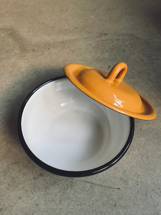 White and mustard yellow enamel pot with a yellow lid on a concrete surface