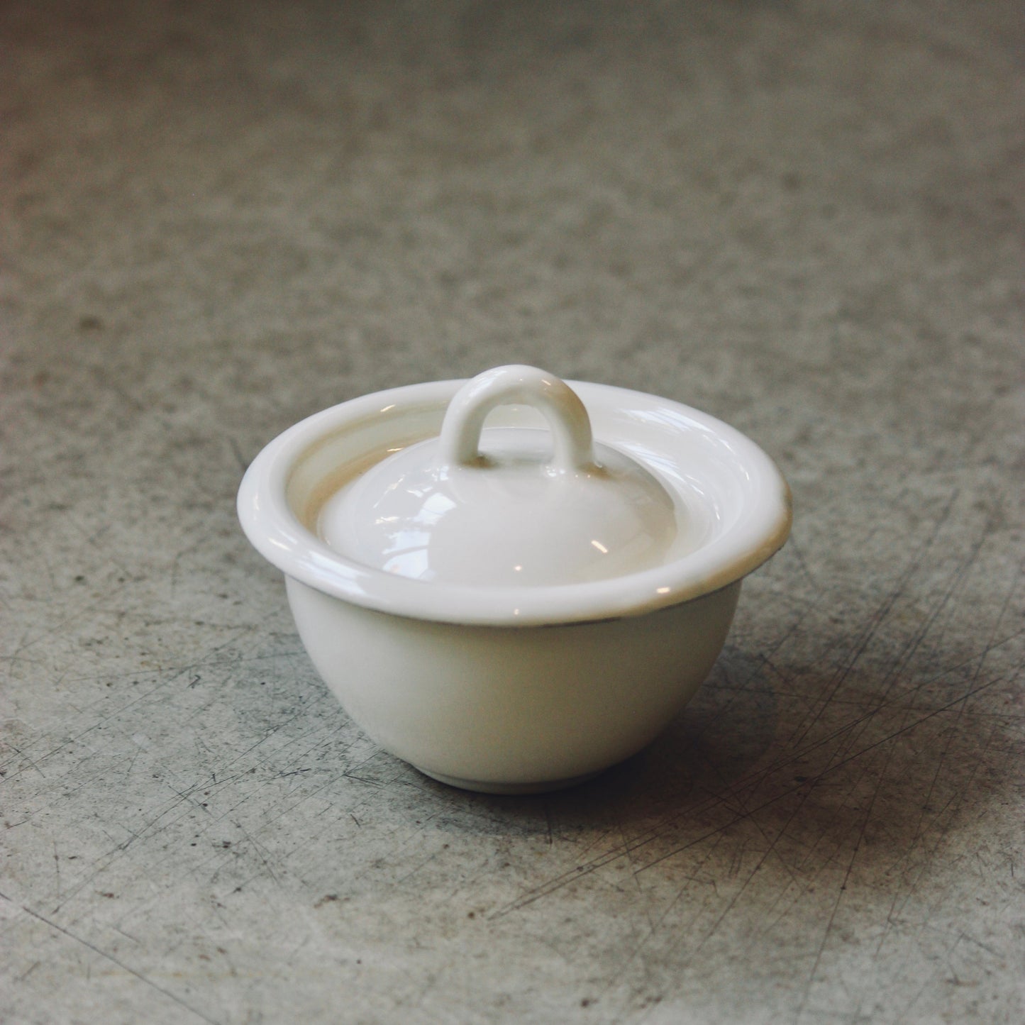 White enamel bowl with lid on a textured surface
