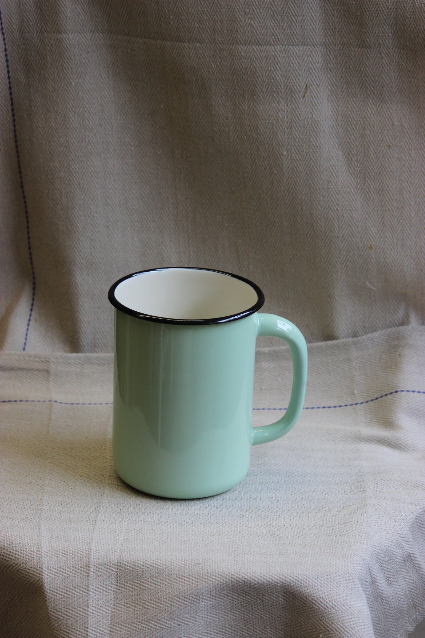 Light green jug with a black rim on a beige fabric background
