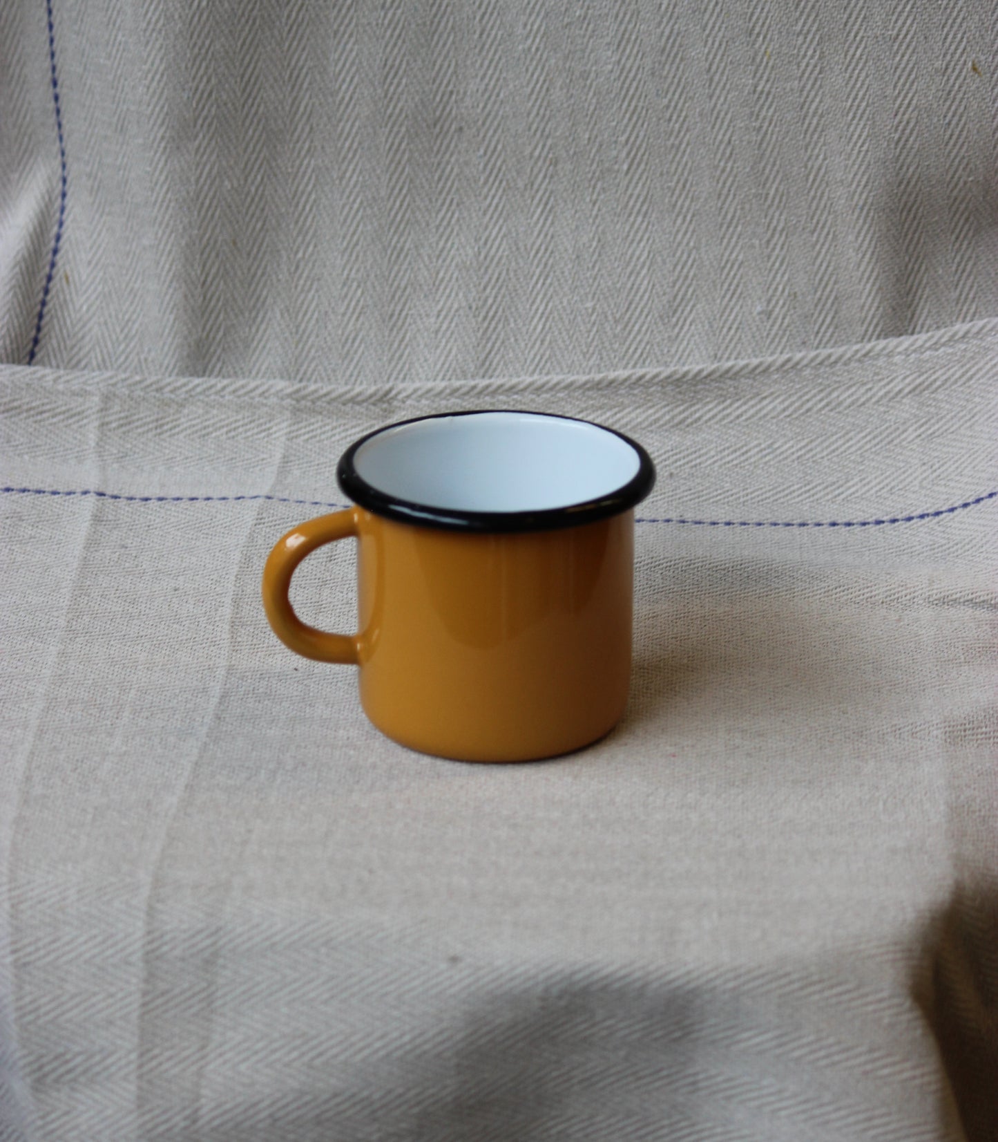 Yellow mug with black rim on a textured fabric surface