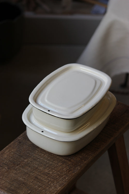 Two white enamel casserole dishes on a wooden surface