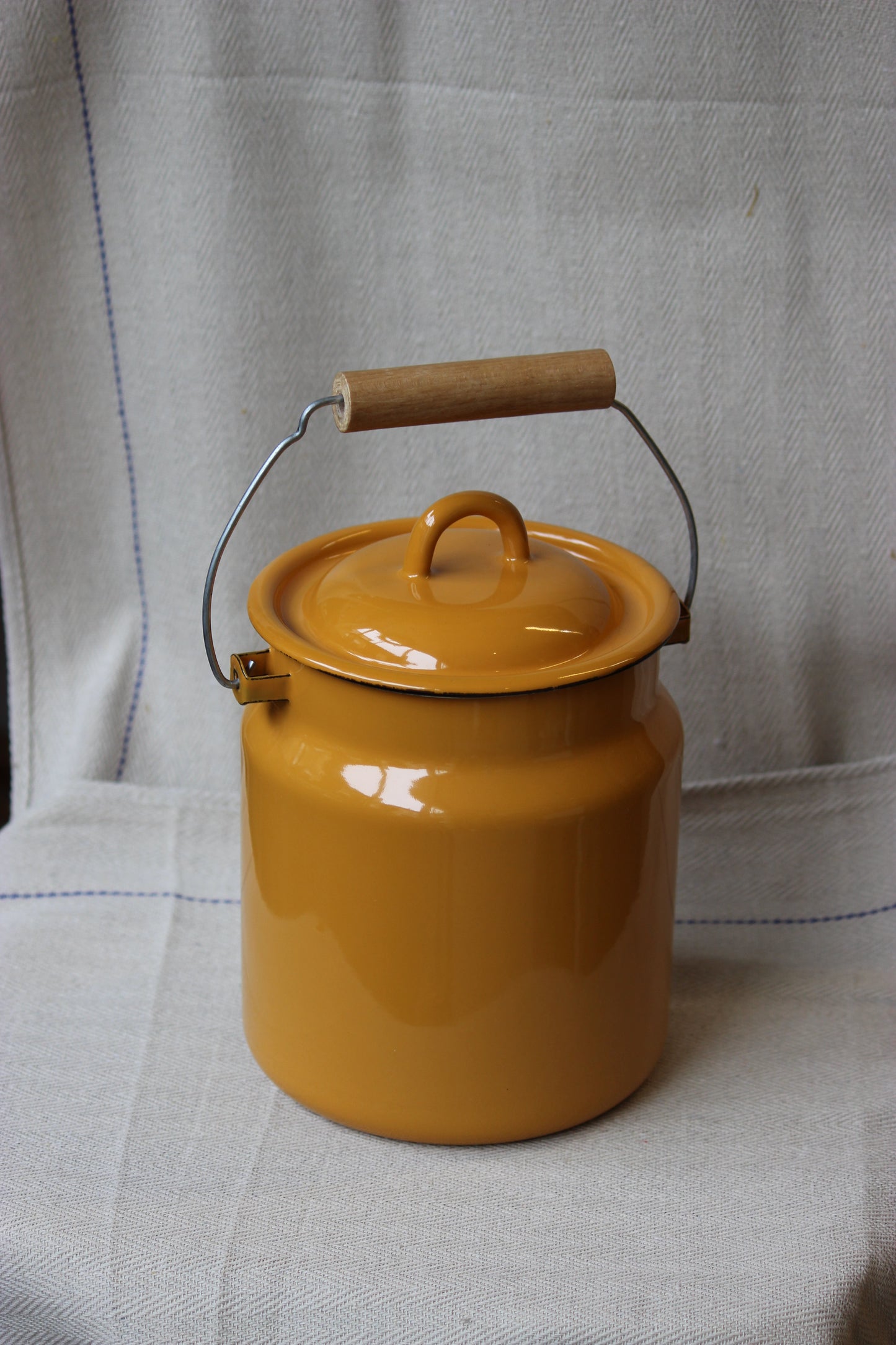 Yellow enamelware pot with a lid on a gray fabric background