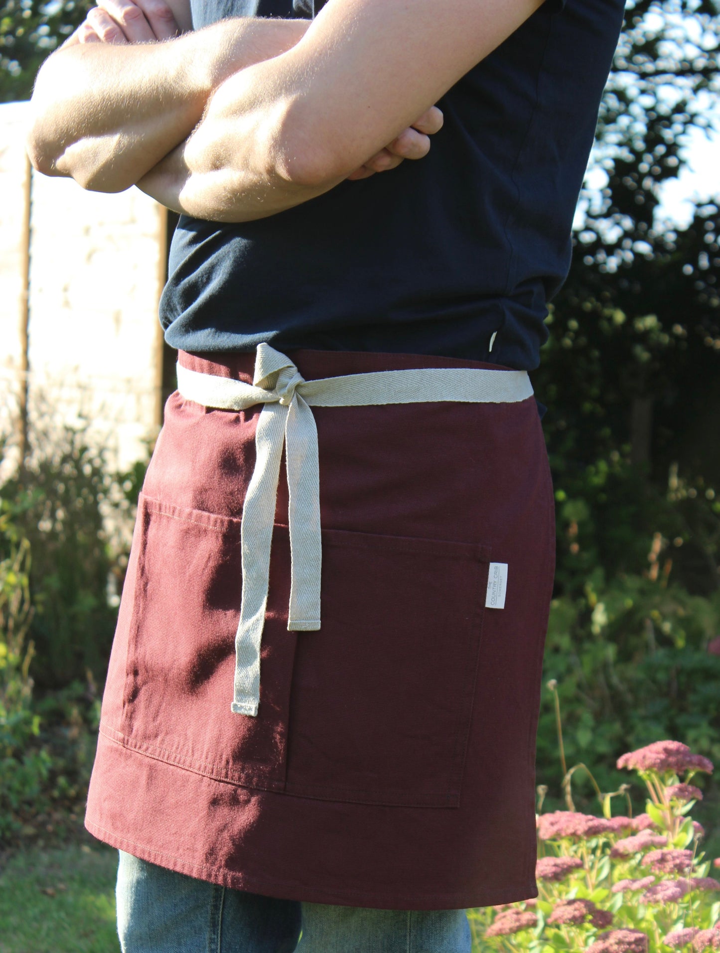 Person wearing a maroon apron with a white strap in an outdoor setting