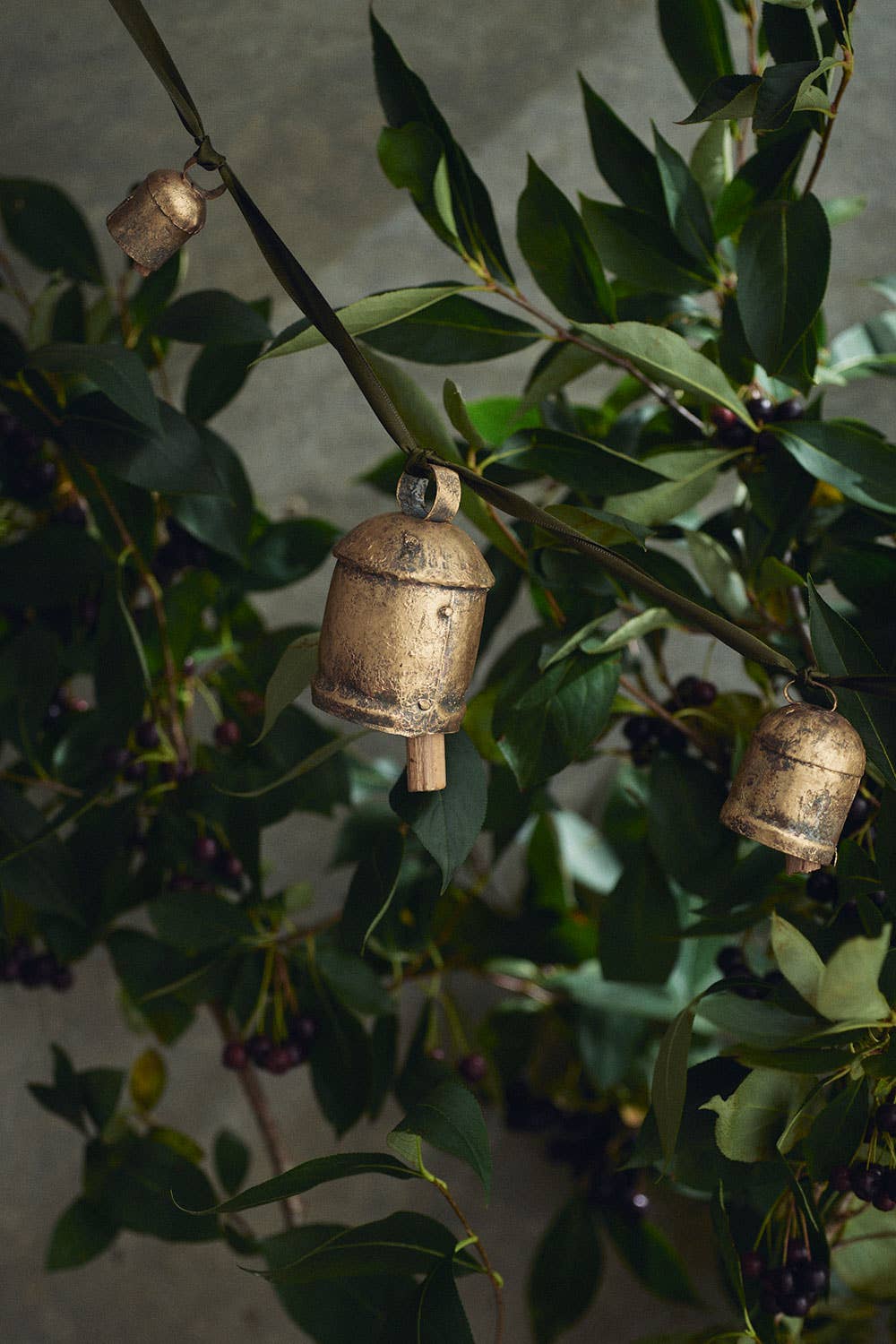A bronze colored metal bell ornament hanging among green leaves, likely used as a Christmas decoration.
