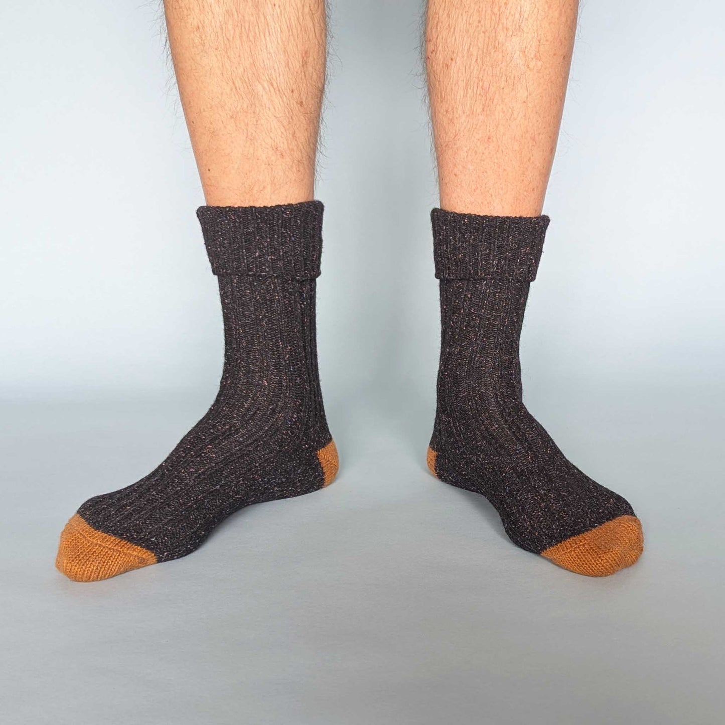 Dark brown socks with orange toes and cuffs worn by a person on a light gray background