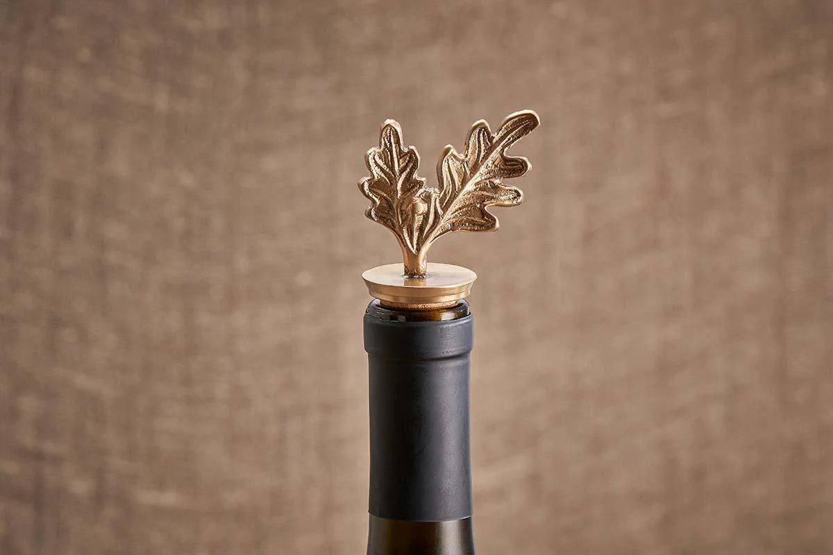 A brass bottle stopper in the shape of an oak leaf, placed on a wine bottle cork.