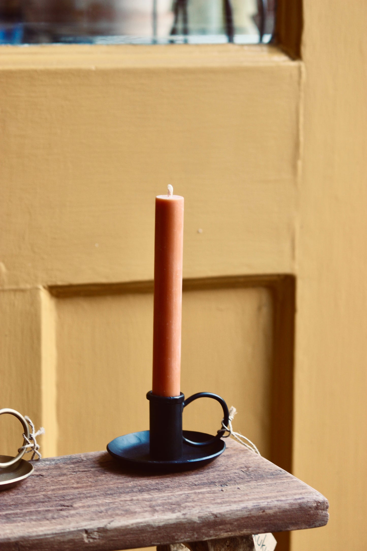 dinner candle in a nkuku black holder on a wooden surface with a mustard door background at The Country Crib