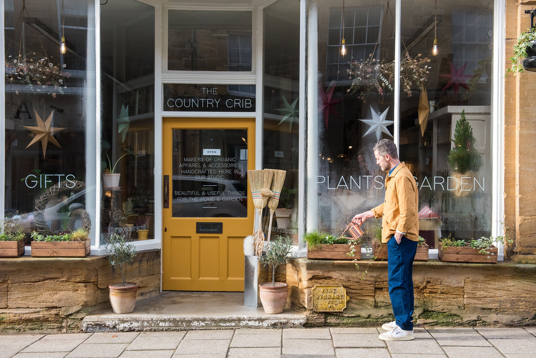 The shop front of The Country Crib in Sherborne with a gentleman watering plants on the windowsill