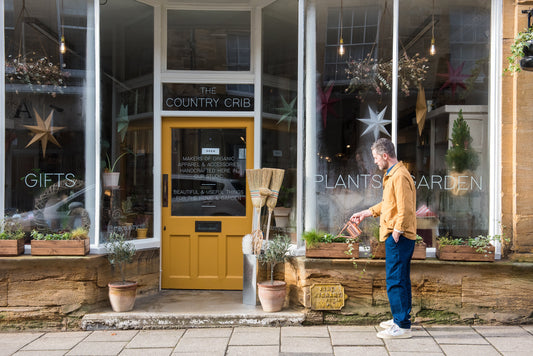 The shop front of The Country Crib in Sherborne with a gentleman watering plants on the windowsill