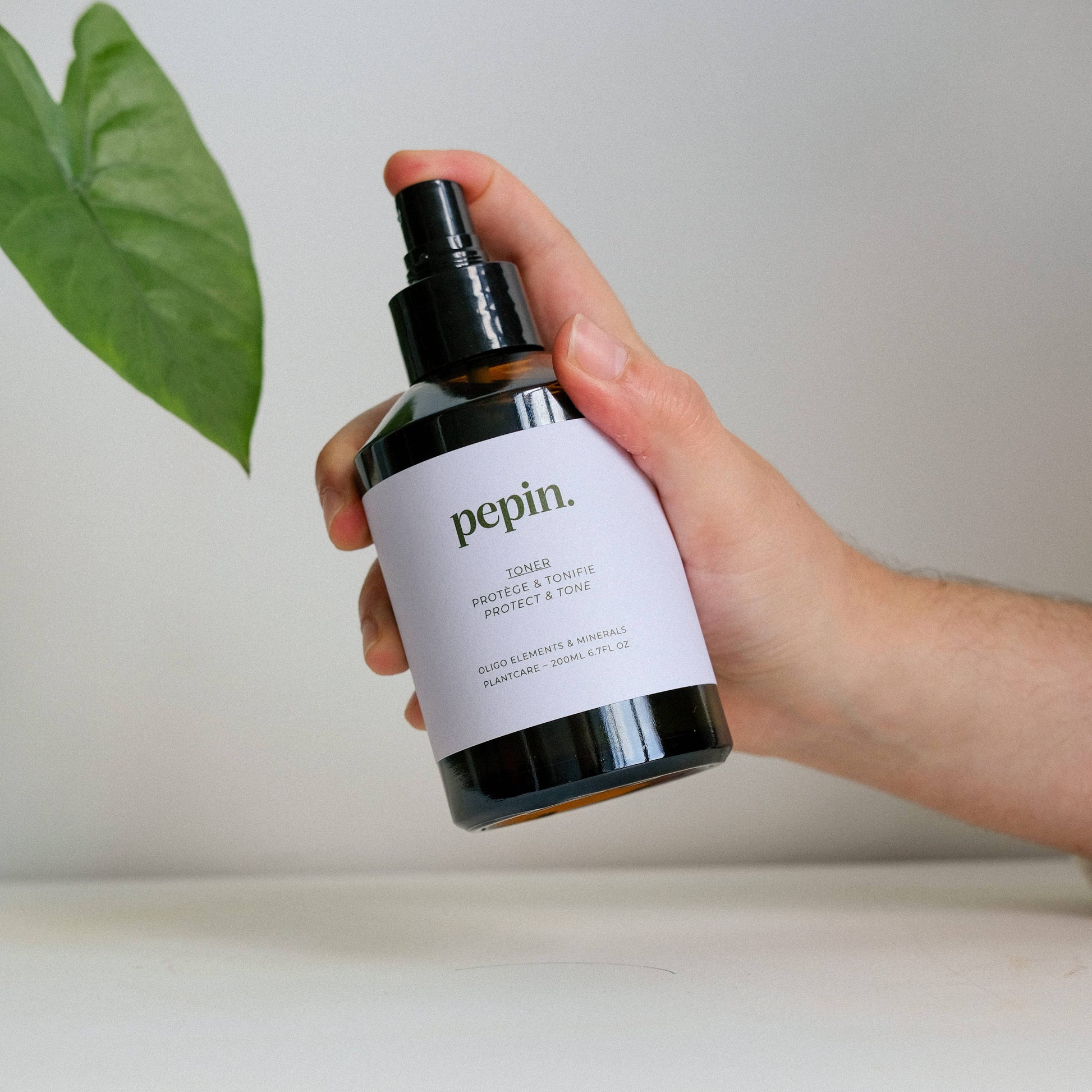 Hand holding a skincare bottle labeled 'pepin' with a leaf in the background
