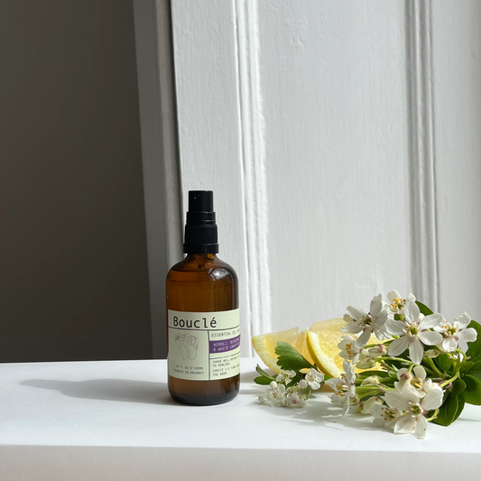 Bottle of Boucle product on a white surface with lemon slices and flowers.