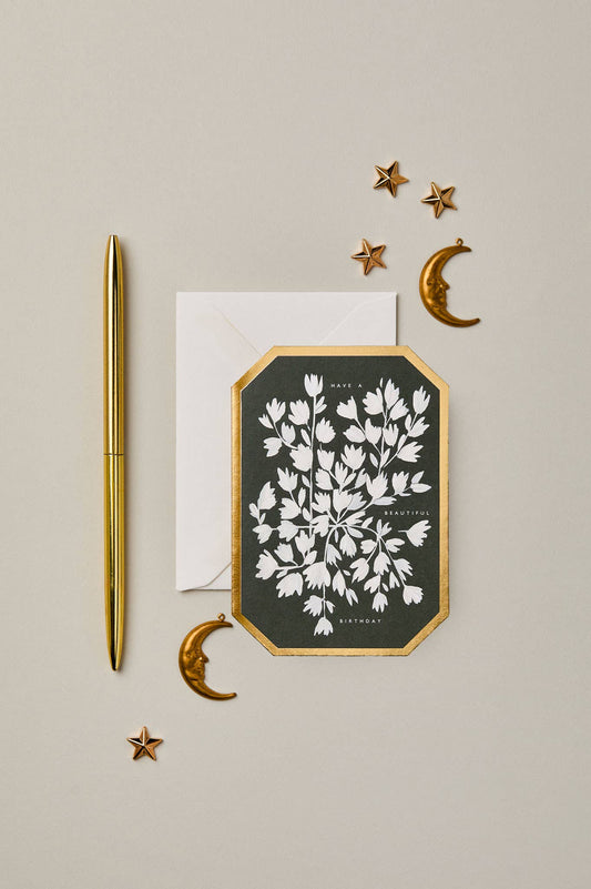 Decorative card with floral design, gold pen, and celestial elements on a beige background