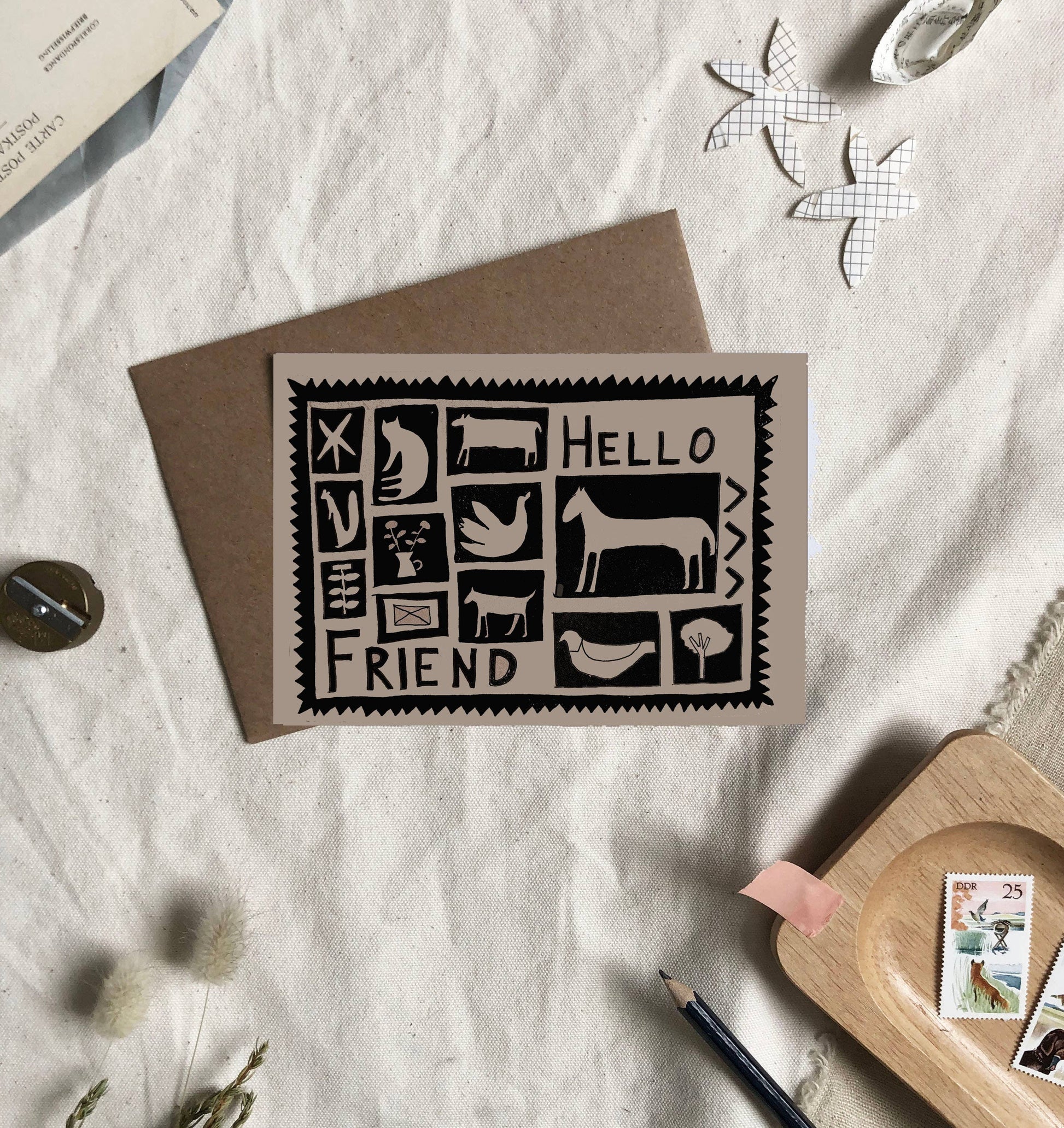 Greeting card with 'Hello Friend' design on a textured surface with stationery items.