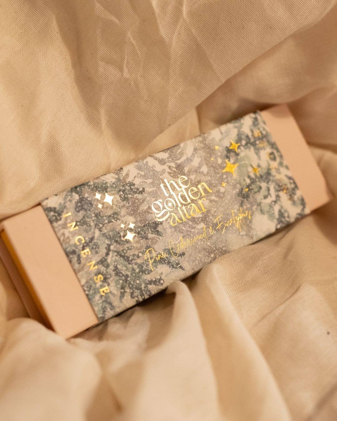 The Golden Altar Incense box with decorative label on a beige fabric background
