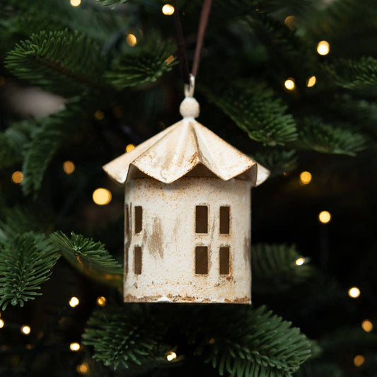Decorative house ornament hanging on a Christmas tree with lights in the background