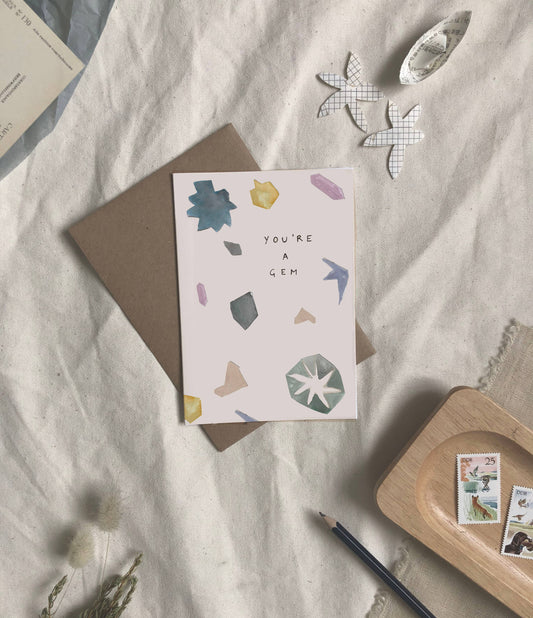 Greeting card with geometric designs and text on a textured surface with stationery items.