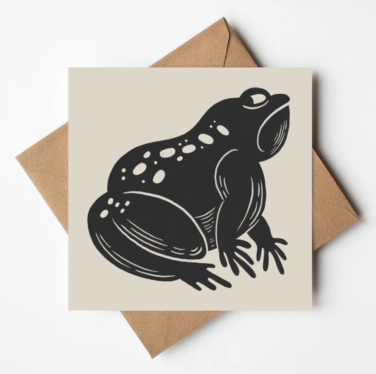 Card with a black frog illustration on a beige background, placed on a brown envelope.