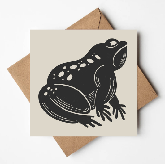 Card with a black frog illustration on a beige background, placed on a brown envelope.
