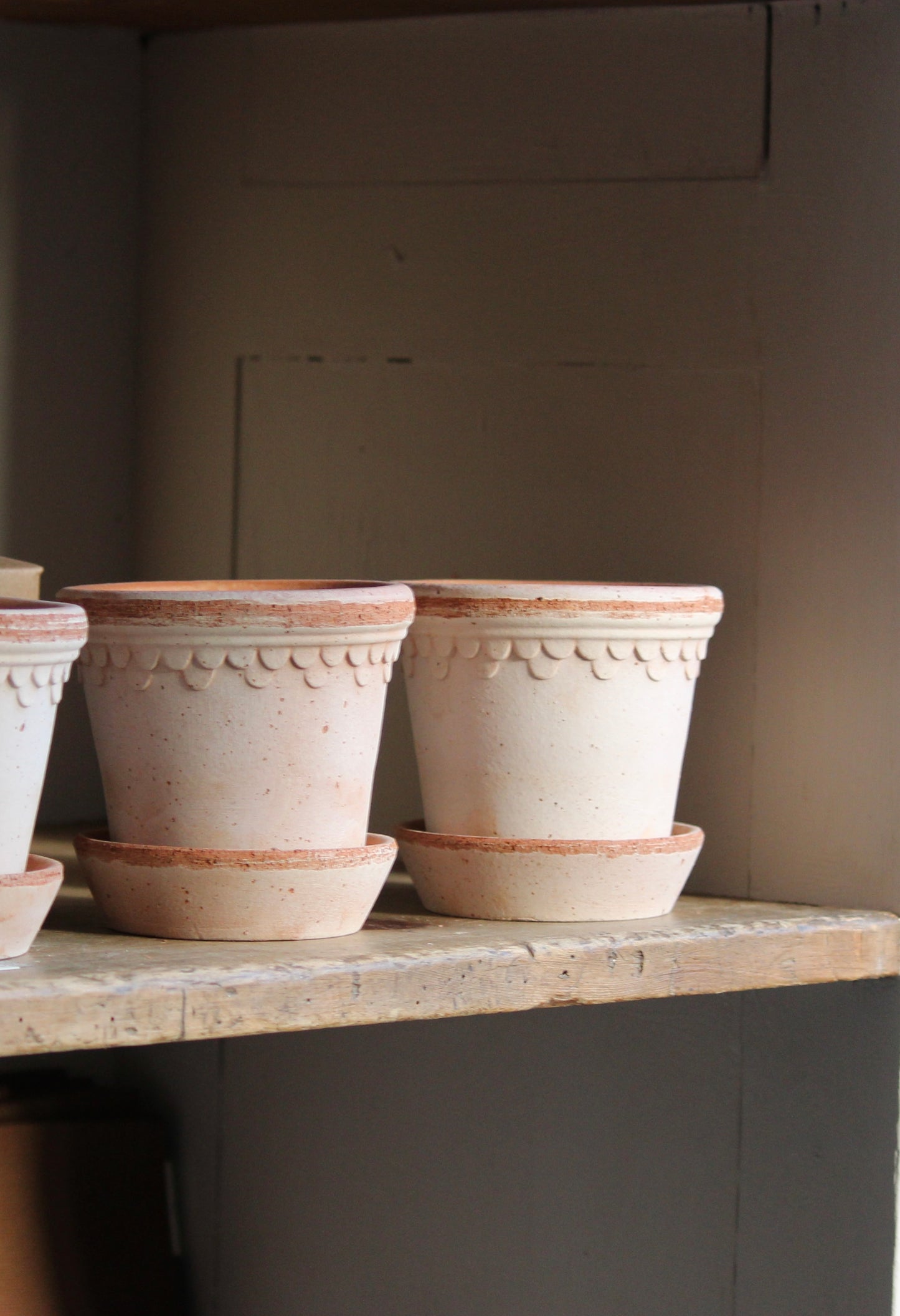 A row of beige terracotta pots with decorative patterns, placed on a wooden shelf.