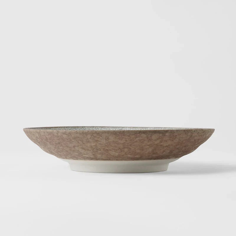 A wide, shallow ceramic bowl with a textured, speckled brown exterior and a smooth, off-white glazed base, photographed against a clean, light gray studio background. Ceramic bowl with textured surface on a white background. Crazed Grey Shallow Bowl made in Japan 