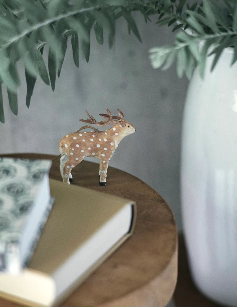 Small deer figurine on a book with a plant and vase in the background