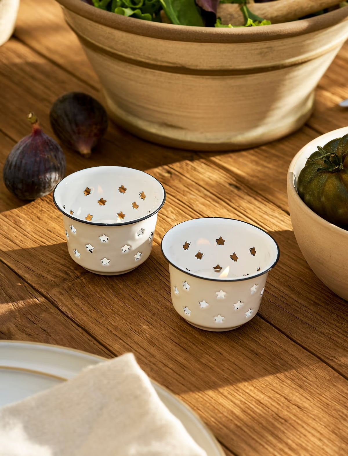 Two white ceramic tealight candle holders with star patterns on a wooden surface.