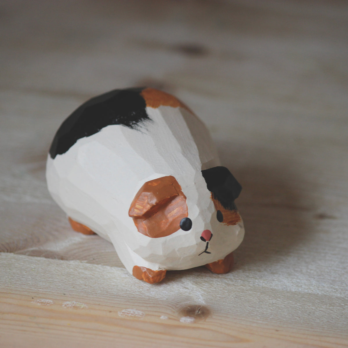 A hand-carved wooden guinea pig figurine with painted black, white, and orange fur, resting on a light wood surface.