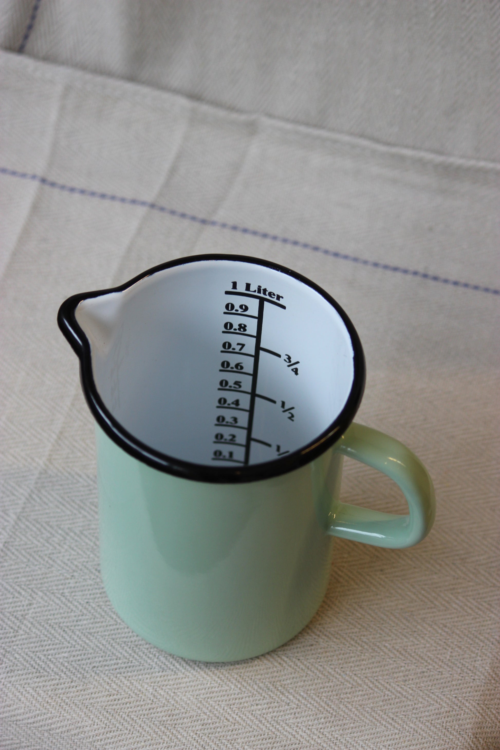 Green measuring jug with a black measurement scale on a beige fabric background