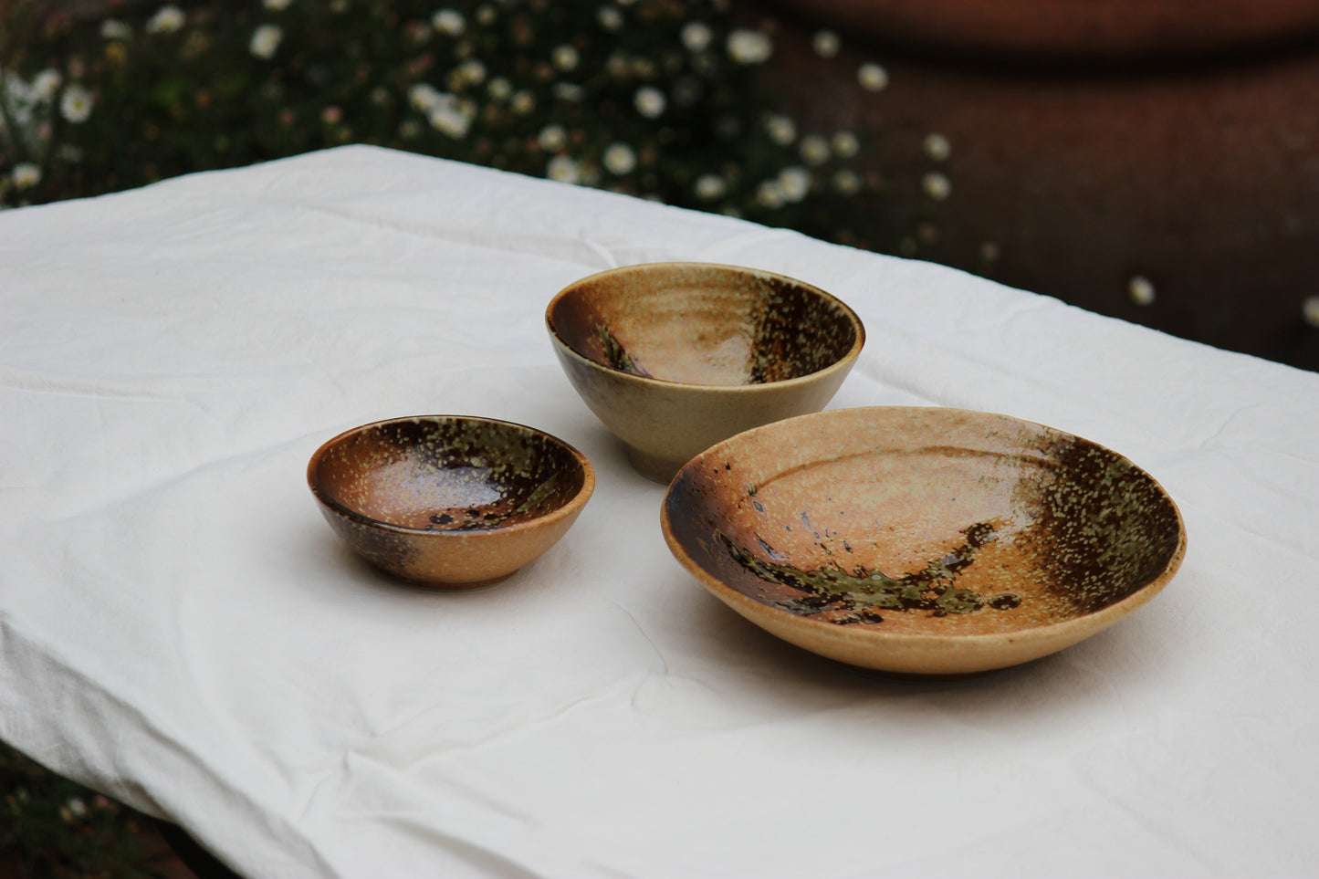 Three WABI SABI ceramic bowls with a rustic finish on a white cloth.