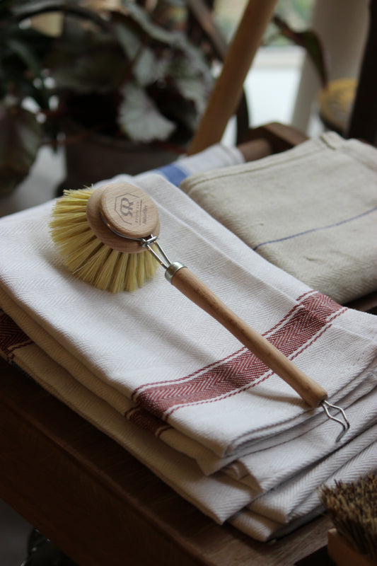 Cleaning brush with wooden handle and green bristles hanging on a white towel.