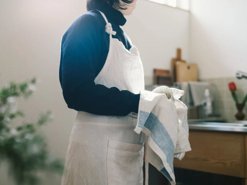 Person wearing a blue sweater and white apron in a kitchen setting.