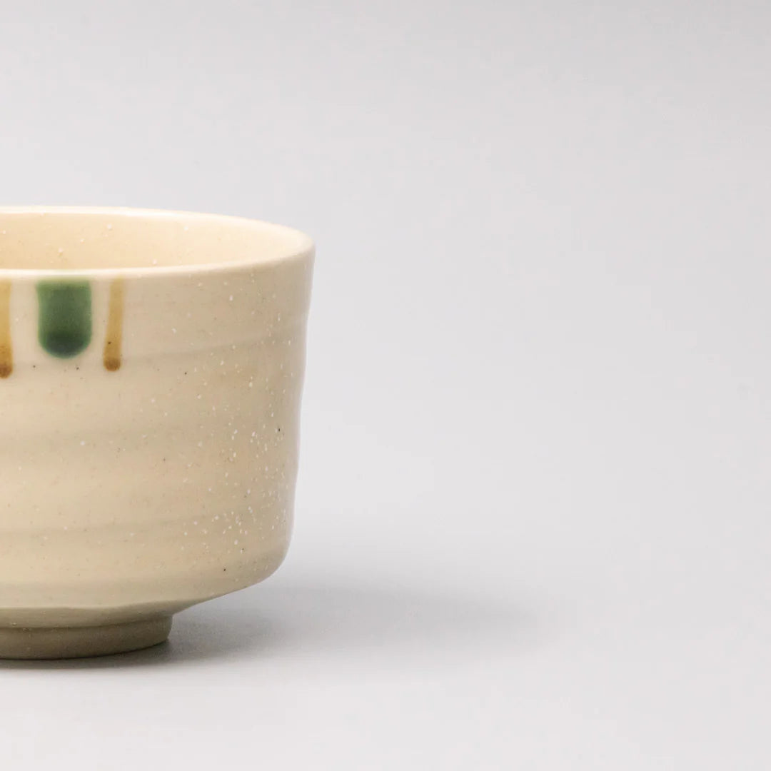 Close-up of a ceramic cup with speckled texture and green and brown accents on a light gray background