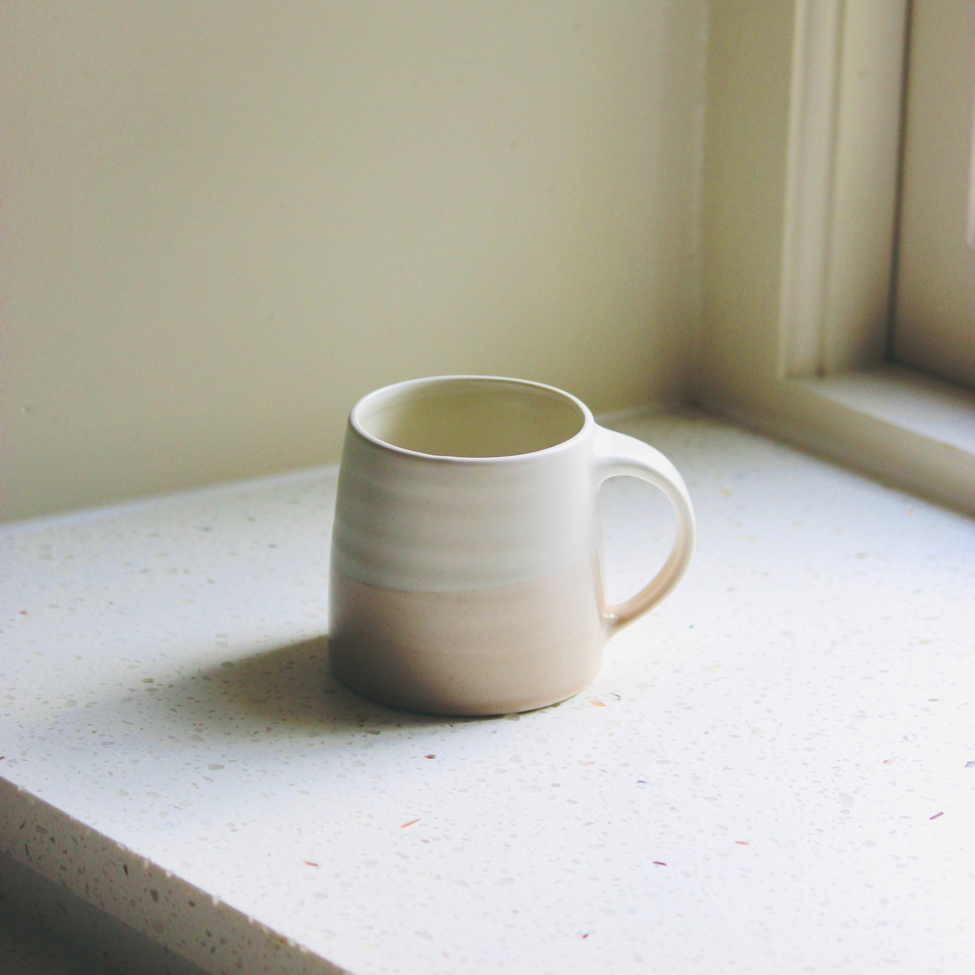White ceramic KINTO mug on a windowsill with soft lighting